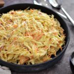 Skål med coleslaw som innehåller strimlad vitkål och morötter i en krämig dressing.