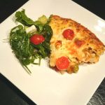 En skiva grekisk bondomelett serverad med en sallad på en vit tallrik.