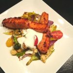 Grillad laxfilé serverad med blandade grönsaker och en vit sås på en vit tallrik.