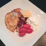 En tallrik med stekt ägg, bacon, ostskivor, körsbärstomater och keso.