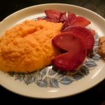 Tallrik med rotmos, röda äpplen och en bit kött på en mönstrad tallrik.