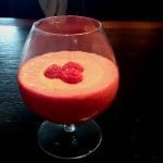 Smoothie med hallon och lakrits i ett klart glas, dekorerad med hallon på toppen.