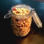 Glasburk med glutenfri müsli fylld med nötter och frön på en mörk yta.