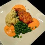 Panerad torskfilé serverad med potatismos och gröna ärtor på en vit tallrik.