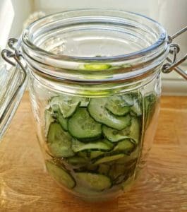 Glasburk med skivade gurkor inlagda i vätska, placerad på en träyta.