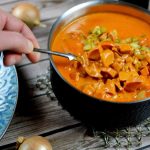 En hand som rör om i en gryta med korv stroganoff, innehållande korvbitar och grönsaker.