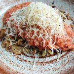Tallrik med pasta täckt av tomatsås och riven ost, serverad på en brun och vit mönstrad tallrik.