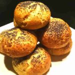 En hög av hembakade bröd med vallmofrön på toppen, placerade på en vit tallrik.