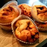 En samling av kanelbullar i pappersformar placerade på en träskärbräda.
