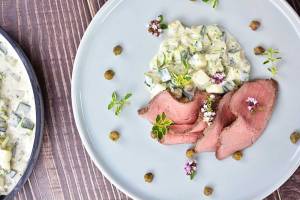 Tallrik med skivad kött och potatissallad dekorerad med örter och blommor.