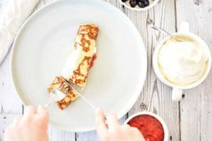 En pannkaka på en tallrik med bärsås och grädde i skålar bredvid.