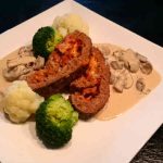 Köttfärslimpa skivad och serverad med sås, broccoli och blomkål på en vit tallrik.