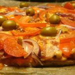 En LCHF pizza med tomater, lök, paprika och gröna oliver på en bakplåt.