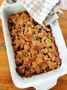 Rabarberpaj med krispigt täcke i en vit ugnsform på ett träbord.