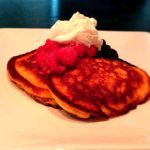 Två amerikanska pannkakor med bär och vispad grädde på en vit tallrik.