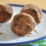 Fyra chokladtrufflar rullade i kakaopulver på en vit tallrik.