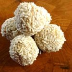Fem bollar av Raffaello med kokosflingor på en träyta.