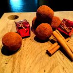 Jultryfflar i chokladpulver och kanelstänger på en träskärbräda med små röda presentförpackningar.
