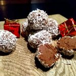 Kokostryffel rullad i kokos med några röda presentförpackningar på en träskiva.