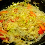 En stekpanna med grönsaksstekt fettuccine och skivade grönsaker som tomater och kål.