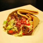 En tortilla fylld med kött, grönsaker och sås på en vit tallrik.