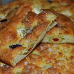 Focaccia med oliver och fetaost, skuren i bitar och dekorerad med örter.