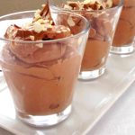 Tre glas med mejerifri chokladmousse toppad med hackade nötter på en vit tallrik.