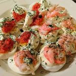 Tretton ägghalvor med räkor och röd kaviar på en vit tallrik, dekorerade med dill.