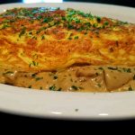 Fransk omelett serverad med en krämig champinjonstuvning på en vit tallrik.