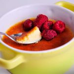 En skål med sockerfri crème brûlée toppad med hallon och en sked.