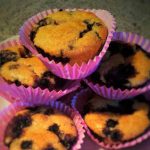 Fem blåbärsmuffins i rosa pappersformar staplade på en tallrik.