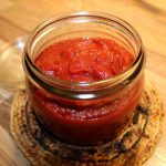 En glasburk med hemgjord ketchup som ligger på en träyta.