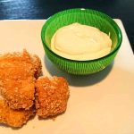 Tre kycklingnuggets på en tallrik med en grön skål med dipp bredvid.