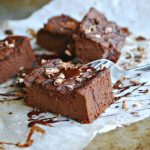 Flera bitar av mjölkfria och mejerifria brownies på ett bakplåtspapper med choklad och nötter.