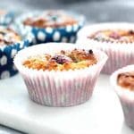 Hallonmuffins i blå och rosa pappersformar på en vit platta.