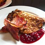 Zucchinipannkaka serverad med skinka och lingonsylt på en vit tallrik.