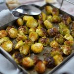 Ugnsstekta brysselkål på en plåt med en grå duk i bakgrunden.