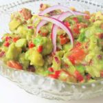 Skål med guacamole som innehåller avokado, tomater, lök och paprika.
