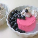 Två skålar med rosa dessert, grädde och blåbär i en neutral miljö.