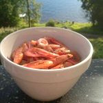 En vit skål fylld med räkor placerad på en yta med utsikt över vatten.