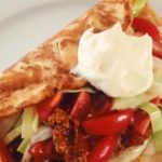Kokostortilla fylld med grönsaker och en klick sås på en tallrik.