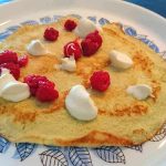 Kokospannkaka på en tallrik med hallon och grädde som dekoration.