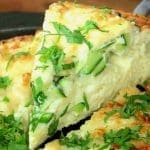 En skiva av zucchini och parmesan frittata med grönsaker och örter på en tallrik.