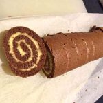 Chokladrulltårta skuren i skivor med vaniljfyllning synlig i mitten.