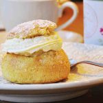 En semla med grädde på en vit tallrik med mönster, med en gaffel bredvid.