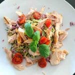 En tallrik med pestokryddade zoodles, kyckling och rostade tomater, dekorerad med basilika.