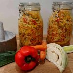 Två glasburkar med inlagda grönsaker, inklusive morötter och paprika, på en träyta.