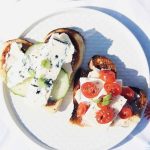 Två skivor rostat bröd med olika pålägg, inklusive gurka, ost och tomater.
