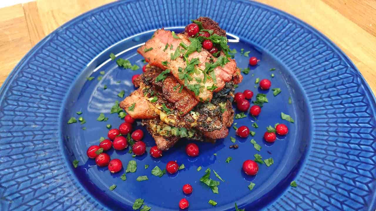 Blomkålsbiffar med parmesan 7 Zucchinibiffar toppade med stekt fläsk och lingon på en blå tallrik.