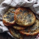En hög av halloumi-bröd med vallmofrön på en vit och röd rutig kökshandduk.